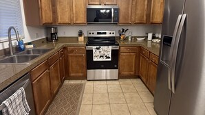 Una cocina con armarios de madera, electrodomésticos de acero inoxidable, piso de baldosas y una ventana con persianas.