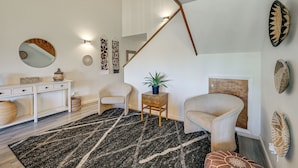 A room with a white console table, a round mirror, a small side table with a plant, a large woven rug, and a chair with a woven backrest. - Near Hiking! Family-friendly Pagosa Springs Haven (Pagosa Springs)