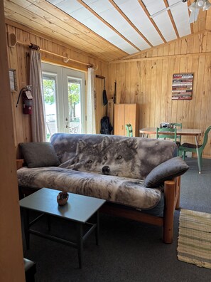 L’intérieur d’une cabane avec un plafond en bois, un canapé à motif de loup, une table, des chaises, un extincteur et un panneau indiquant les règles à respecter dans la cabane.