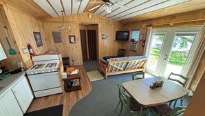 Una cocina compacta con estufa, una mesa de comedor con sillas, un banco y un televisor.