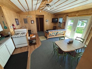 A compact kitchen with a stove, a dining table with chairs, a bench, and a television.