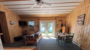 Interior de una cabaña con kitchenette, sofá, mesa de comedor con sillas y ventilador de techo.