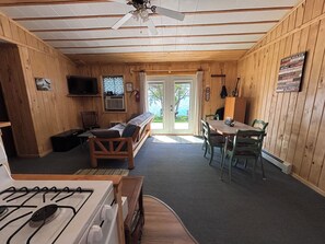 A cabin interior with a kitchenette, a sofa, a dining table with chairs, and a ceiling fan.