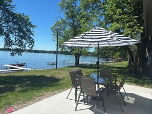 Une terrasse avec une table et des chaises, un parasol à rayures et une vue sur un lac où naviguent des bateaux.