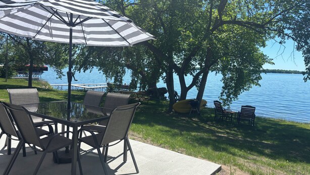 Un patio junto al lago con una mesa, sillas, una sombrilla y un kayak.