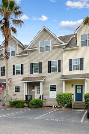 A multi-story residential building with a symmetrical facade, a central entrance with a door, and a small porch area. - Lakefront 3-bedroom townhome with private deck. Prime location! (North Charleston)