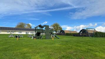 A playground with climbing structures and swings, a picnic table, and a building with a sloped roof in the background.