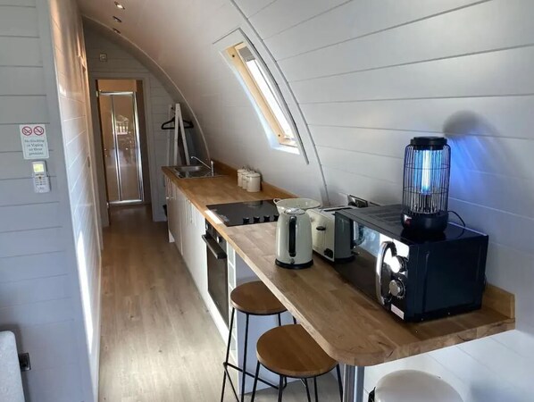A compact kitchen with a wooden countertop, a toaster, a kettle, and a blender.