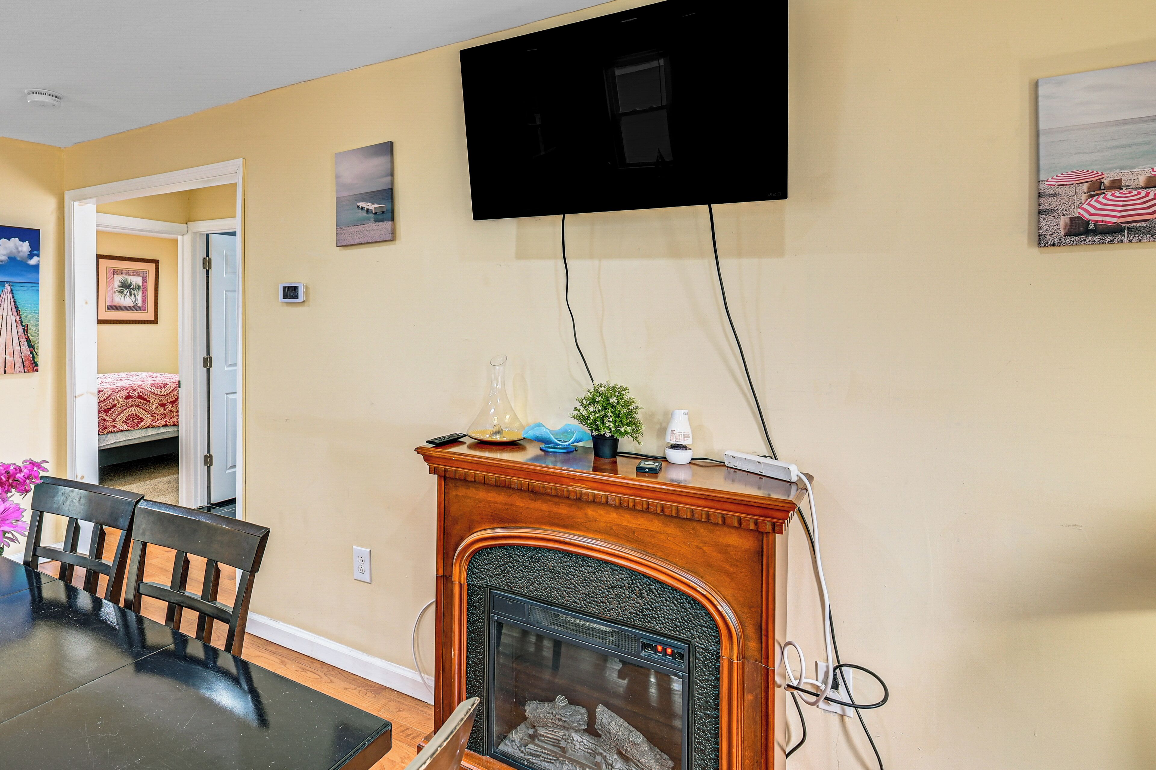 A living room with a fireplace, a television mounted on the wall, and a dining area with chairs.