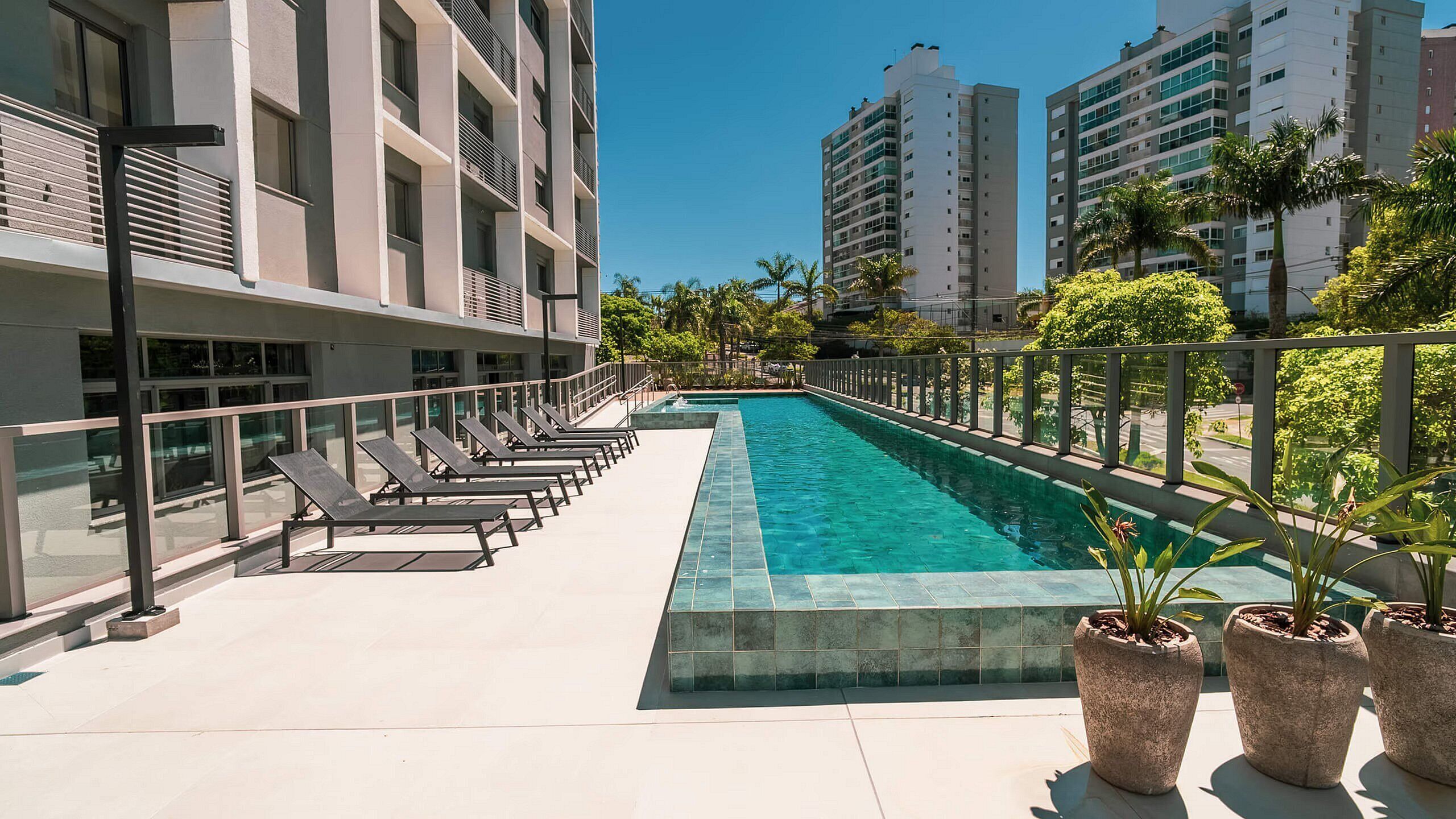 A rooftop pool with lounge chairs, a clear sky, and surrounding high-rise buildings.