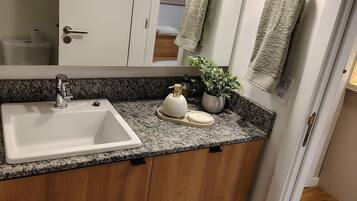 Un baño moderno con encimera de granito, un lavabo blanco, armarios de madera, un espejo y dos luces empotradas.