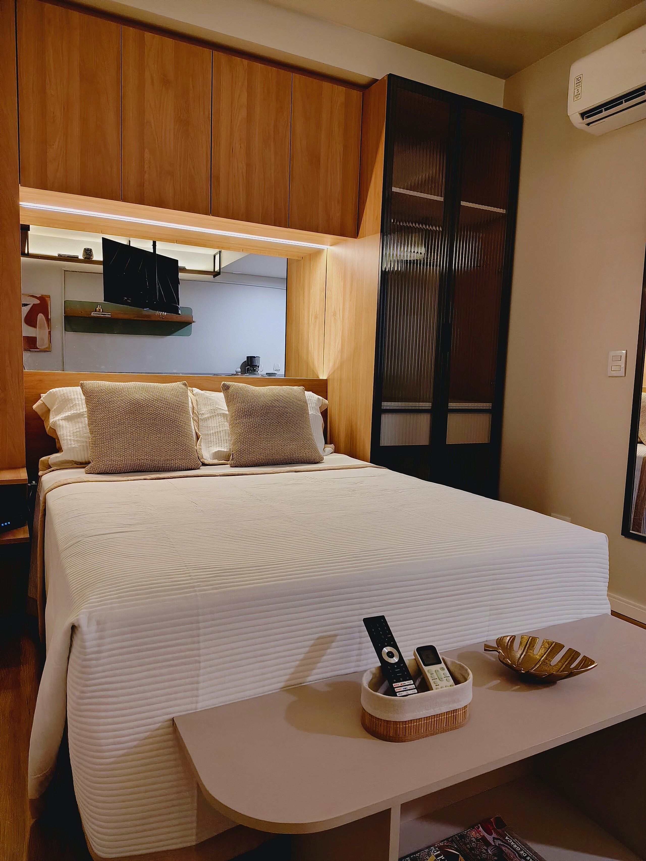 Quarto bem arrumado com cama, mesa de cabeceira e uma pequena estante.
