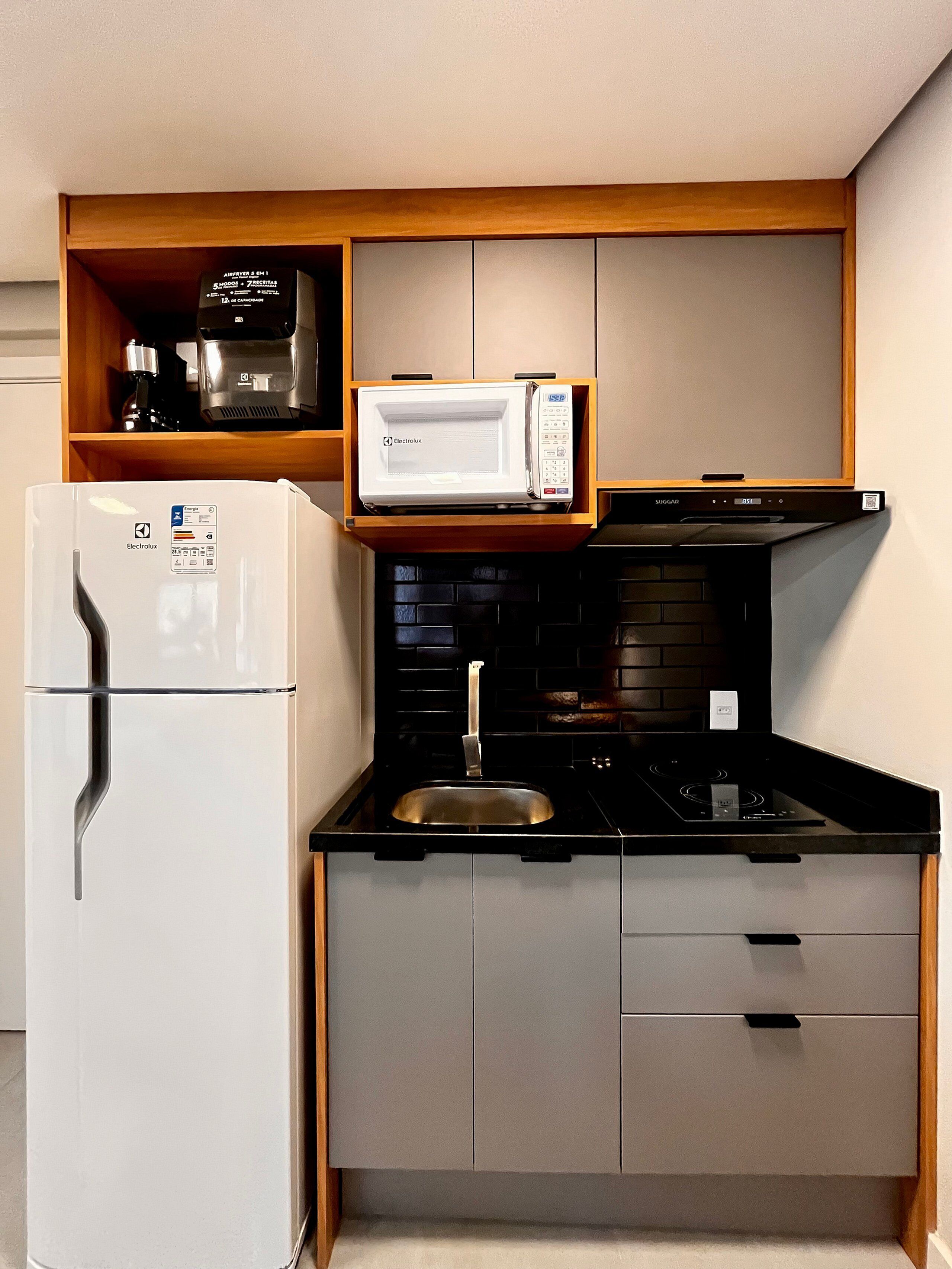 Une cuisine de taille réduite, avec un réfrigérateur blanc, un four à micro-ondes, une cuisinière noire et une étagère en bois placée au-dessus du four à micro-ondes.