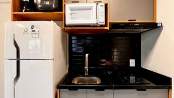 Une cuisine de taille réduite, avec un réfrigérateur blanc, un four à micro-ondes, une cuisinière noire et une étagère en bois placée au-dessus du four à micro-ondes.