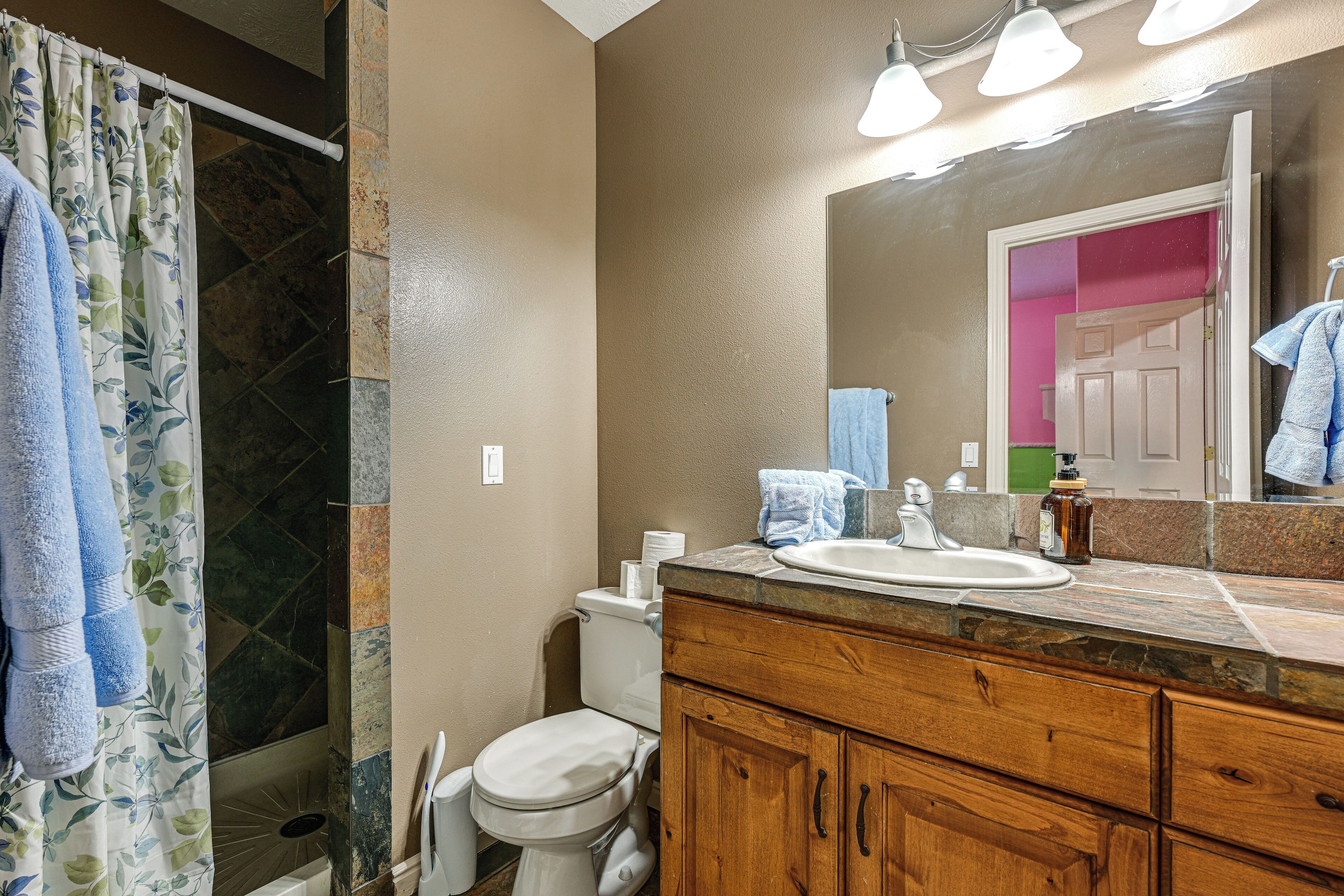 A bathroom with a shower curtain, toilet, sink, and wooden cabinets.