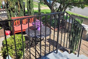 A balcony with a metal railing, a red bench, a round table with a purple vase, and potted plants. - Charming Boutique Home in West End Alexandria! (Alexandria)