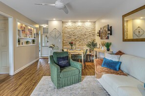 Ein Wohnzimmer mit einem grünen Sessel, einem weißen Sofa, einer Steinwand und einem Essbereich mit Tisch und Stühlen.