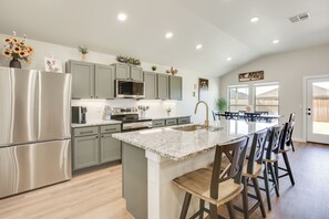 A modern kitchen with a central island, stainless steel appliances, and a dining area with bar stools. - Raiderland Retreat! Family Home 5 Mi to Texas Tech (Lubbock)