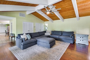 A spacious living room with a sectional sofa, a ceiling fan, and a wooden ceiling.