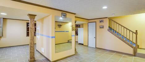 A spacious hallway with a tiled floor, a wooden column, a door, and a staircase with wooden railings.