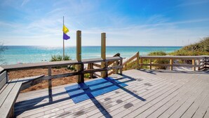 Eine Holzterrasse mit einer blauen Matte, Holzgeländern und einer Fahnenstange mit zwei Flaggen.