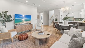 Ein modernes Wohnzimmer mit Flachbildfernseher, rundem Couchtisch und Essbereich mit Stühlen.