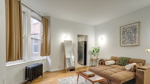 Een woonkamer met een bank, een radiator, een spiegel en een raam met gordijnen.