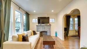 A living room with a fireplace, a sofa, a coffee table, and a view of the outside through large windows. - Walk to Dining & Art: University District Gem! (Detroit)