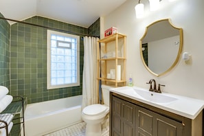 A bathroom with a bathtub, toilet, vanity with a mirror, and a shelf with toiletries. - Walk to Dining & Art: University District Gem! (Detroit)