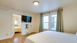A bedroom with a bed, a television mounted on the wall, a window with curtains, and a door leading to another room. - Walk to Dining & Art: University District Gem! (Detroit)