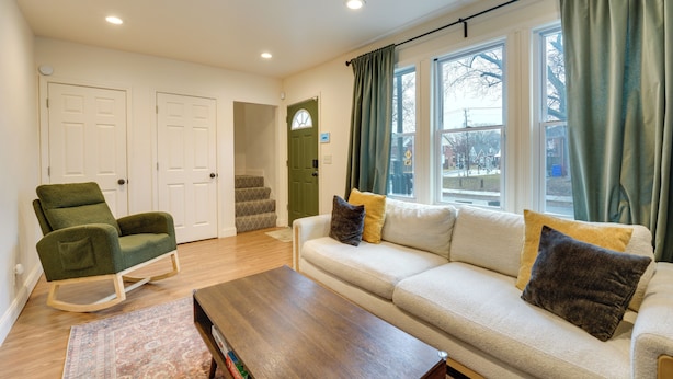 A living room with a sofa, a rocking chair, a coffee table, and a view of the outside through large windows. - Walk to Dining & Art: University District Gem! (Detroit)