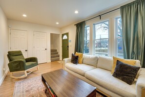 A living room with a sofa, a rocking chair, a coffee table, and a view of the outside through large windows. - Walk to Dining & Art: University District Gem! (Detroit)