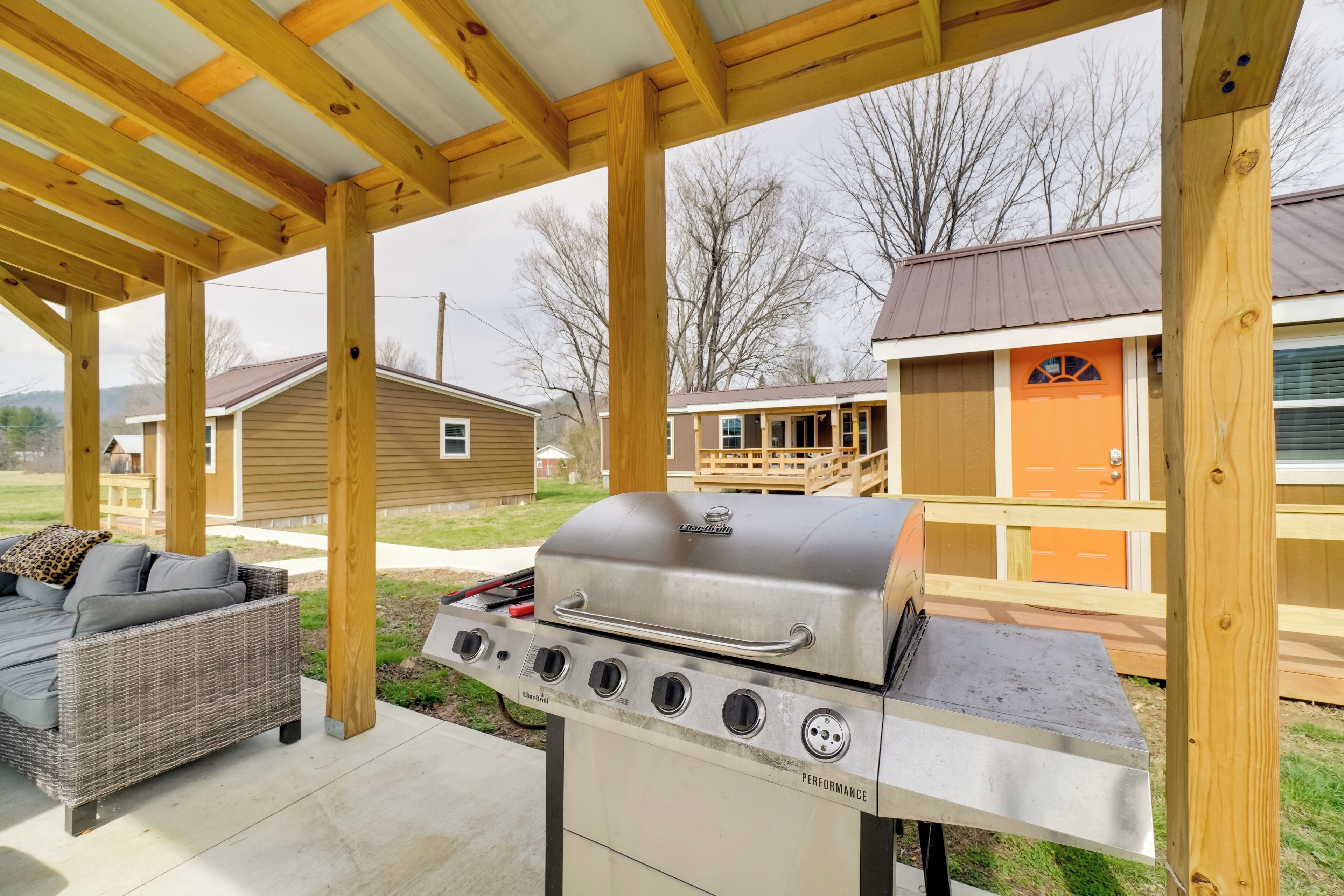 A covered patio with a grill, outdoor furniture, and a wooden deck.