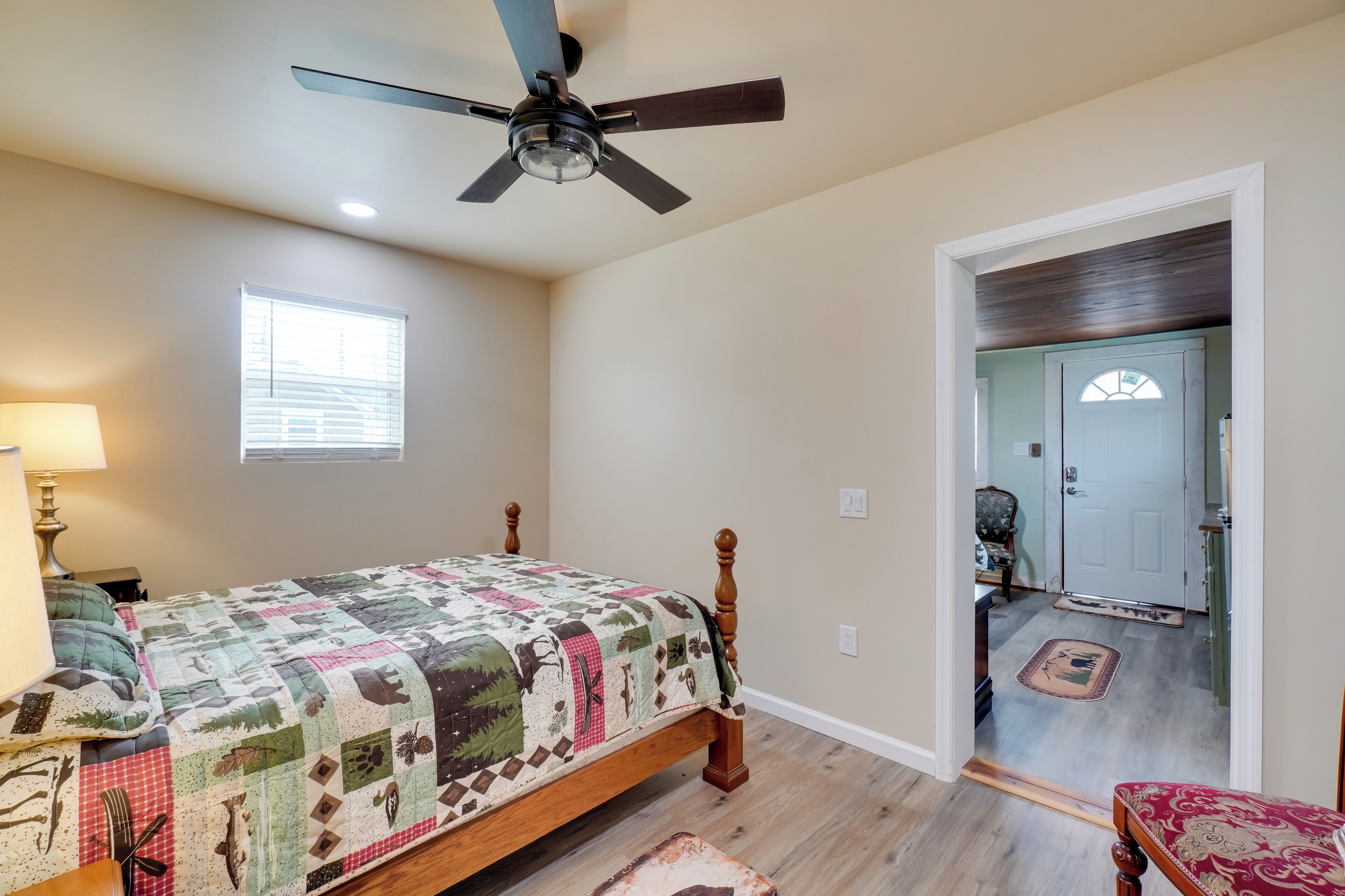 A bedroom with a bed, a ceiling fan, a window, and a door leading to another room.