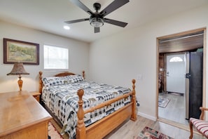 Une chambre à coucher comprenant un lit, un ventilateur de plafond, une lampe, une fenêtre et une porte donnant sur une autre pièce.
