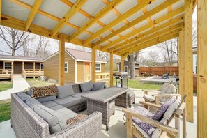 Un porche exterior cubierto con un sofá modular, mobiliario de mimbre y una zona de barbacoa.