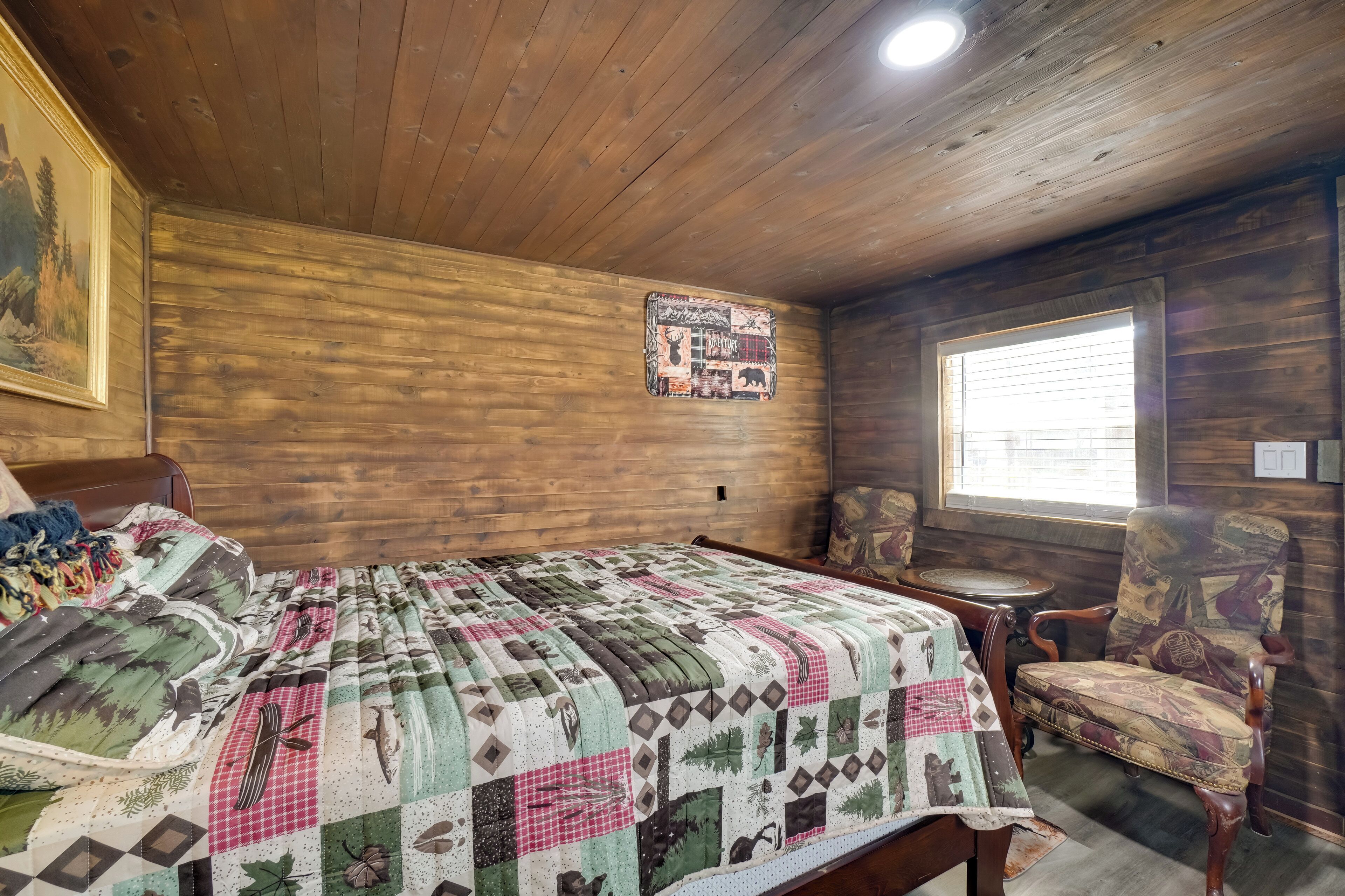 A wooden cabin room with a bed, a chair, a small table, and a window.