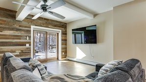 A living room with a ceiling fan, a flat-screen TV, and a large window with a view of trees. - Extended Stay in Skylands! Pet-friendly Retreat (Glenwood)
