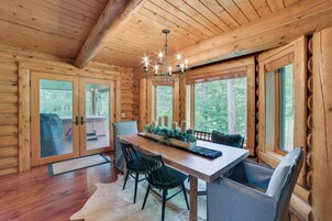Un interior de madera con una mesa de comedor, sillas, una araña y ventanas grandes.