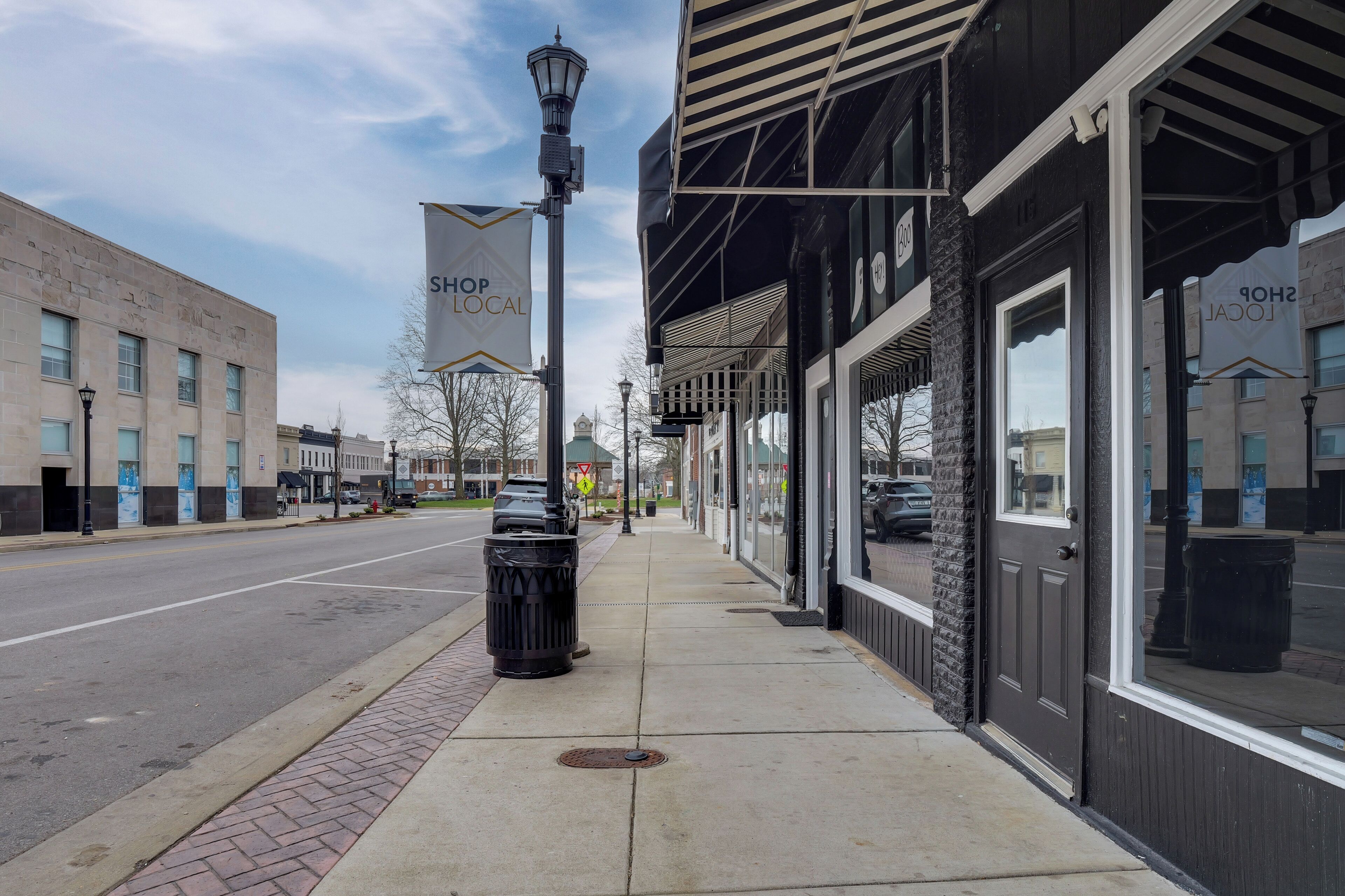 A street with storefronts, a trash can, and a lamp post.