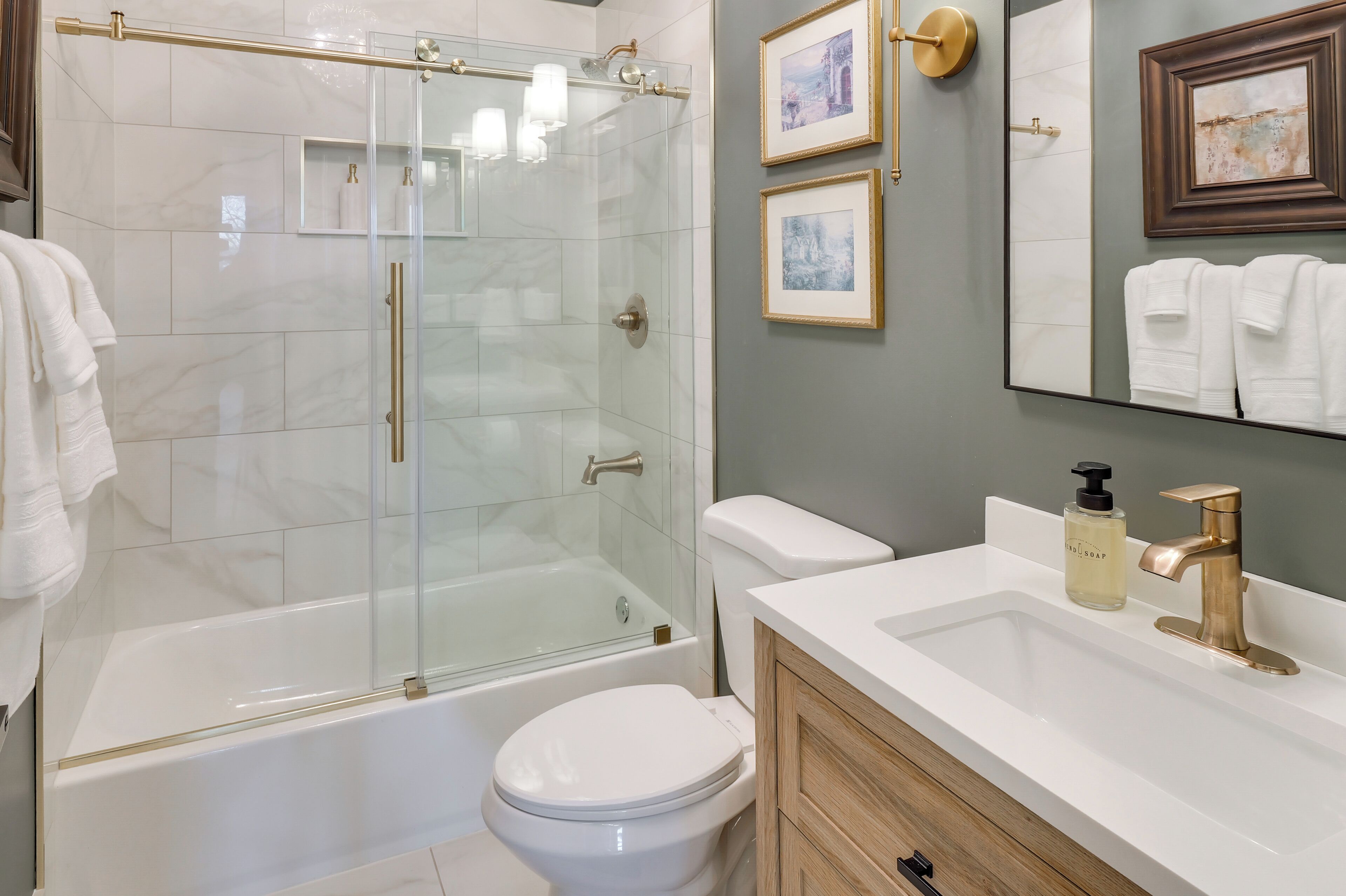 A modern bathroom with a glass-enclosed shower, a white bathtub, a toilet, and a vanity with a sink and a mirror.