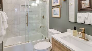 A modern bathroom with a glass-enclosed shower, a white bathtub, a toilet, and a vanity with a sink and a mirror.
