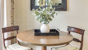 A round wooden table with a white vase and green foliage centerpiece, flanked by two upholstered chairs with wooden frames.