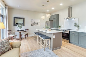 A modern kitchen with a central island, bar stools, wooden chairs, and a dining table.