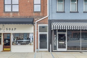 A row of storefronts with a brick building and a blue building, including a shop with a black awning and another with a striped awning.