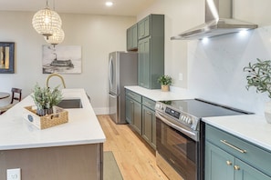 A modern kitchen with a central island, stainless steel appliances, and a chandelier.