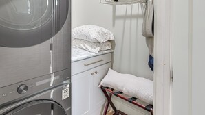 Uma área de lavanderia compacta com máquina de lavar, varal e uma cama pequena com almofadas.