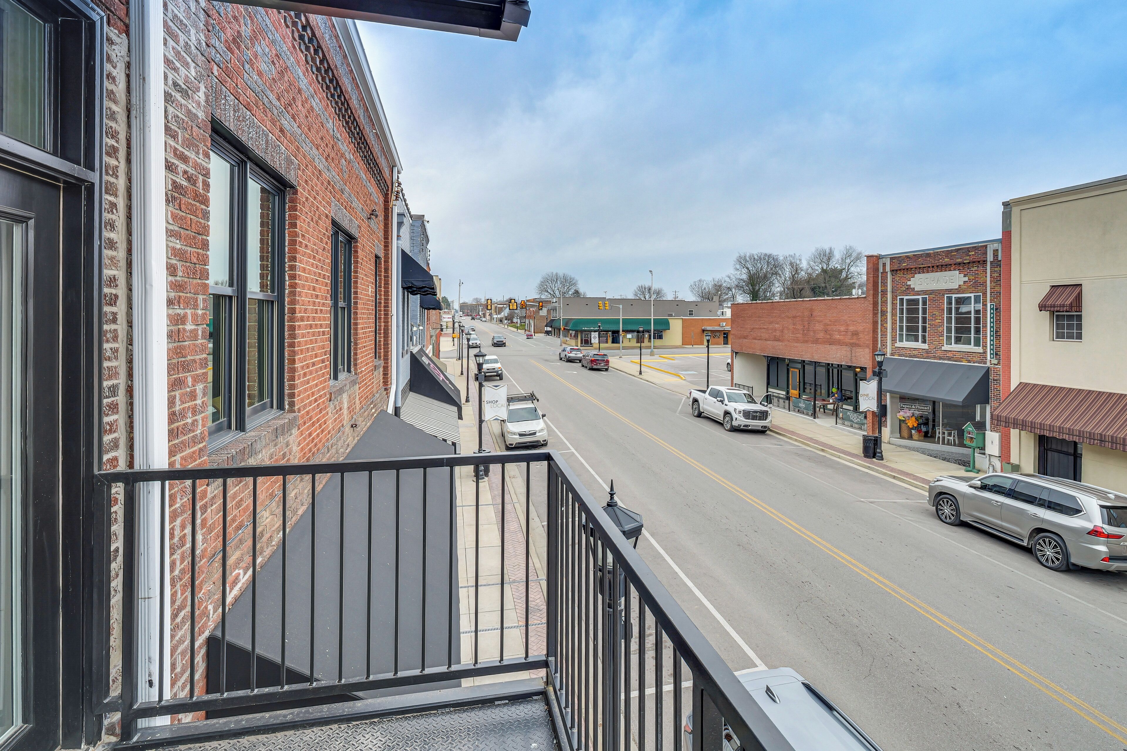 A street view from a balcony overlooking a road with cars, buildings, and a clear sky.