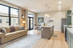 A modern kitchen with a central island, a dining area with a sofa, and large windows.