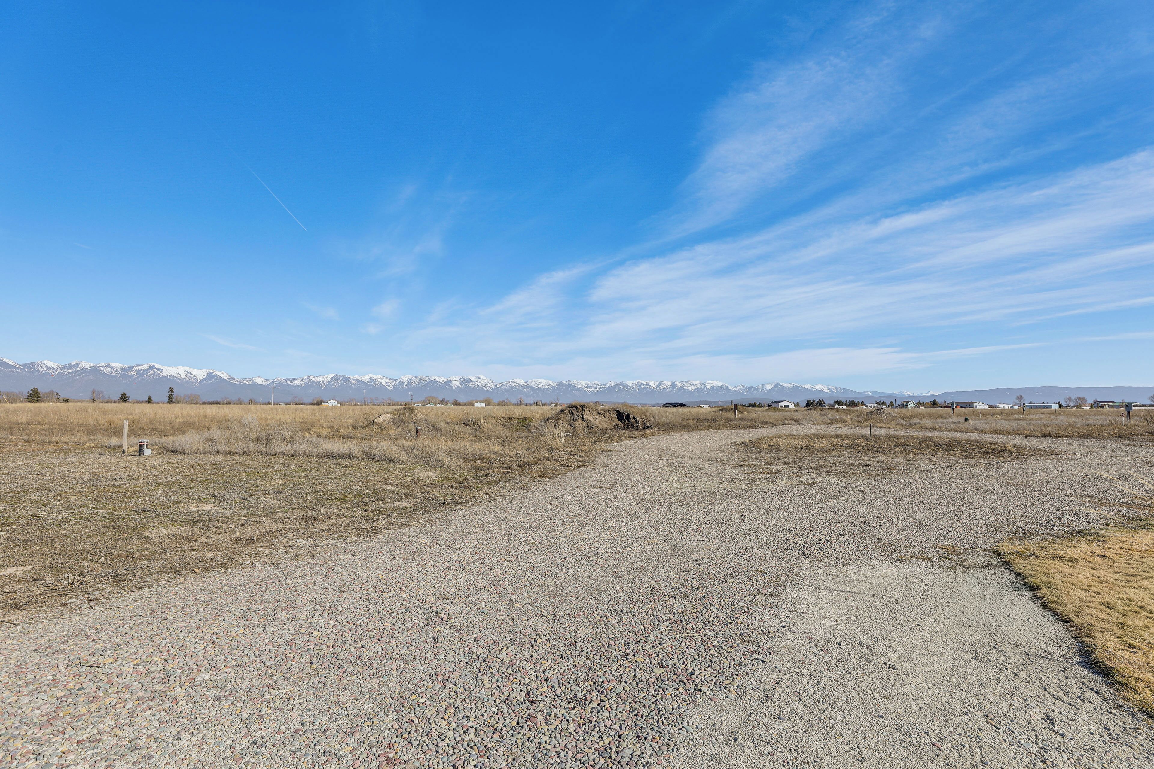 A gravel path leading to a mountainous landscape with snow-capped peaks under a clear sky.